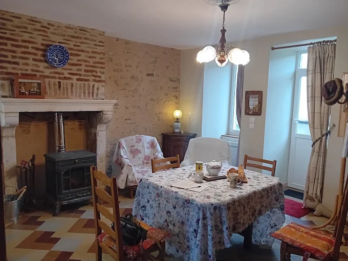 Le séjour du gîte : poêle à bois devant la cheminée en pierre, mur de briques et table dressée